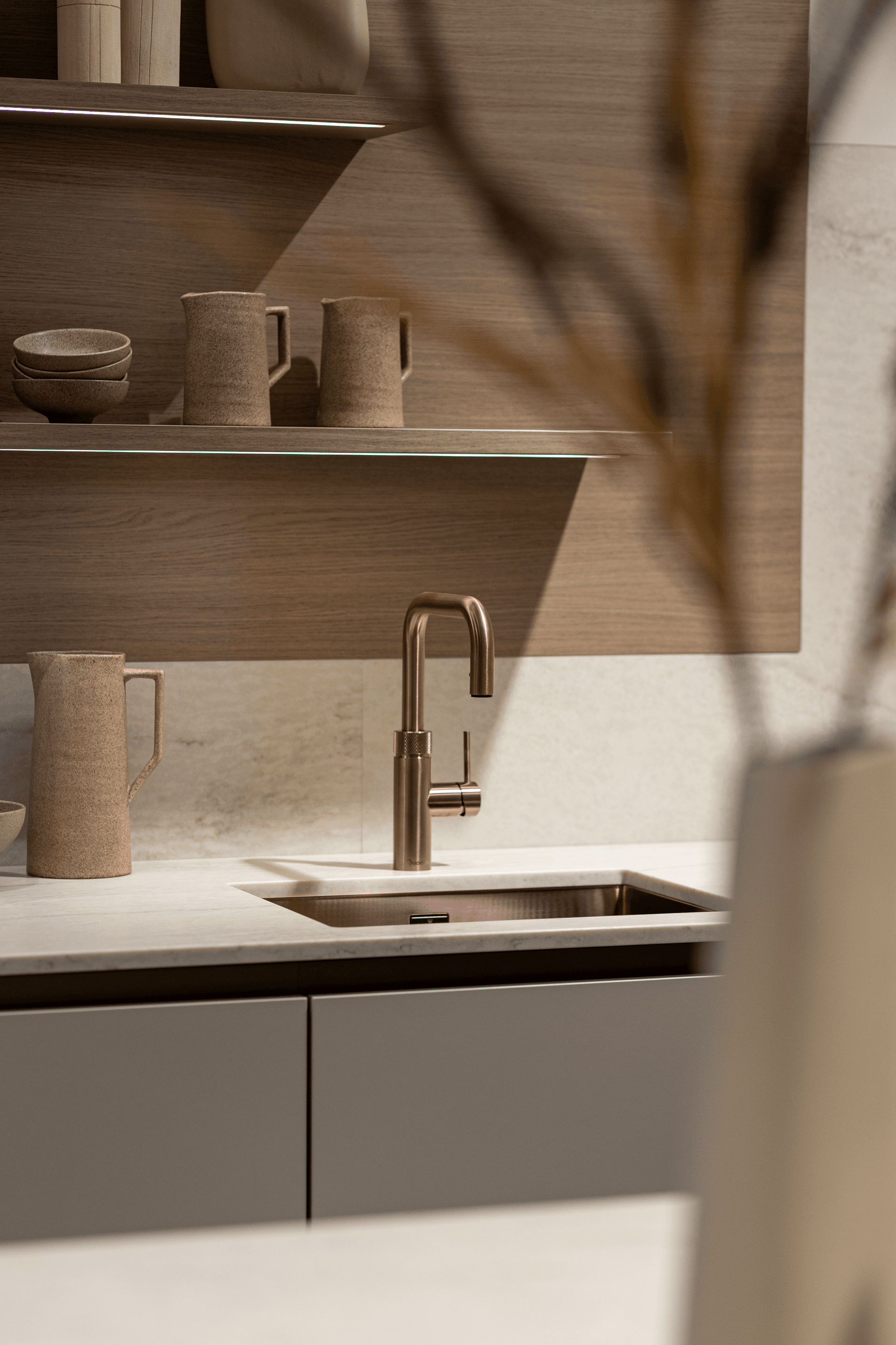 Beige marmer keukenblad, een houten keukenwand en een koperen kraan en spoelbak