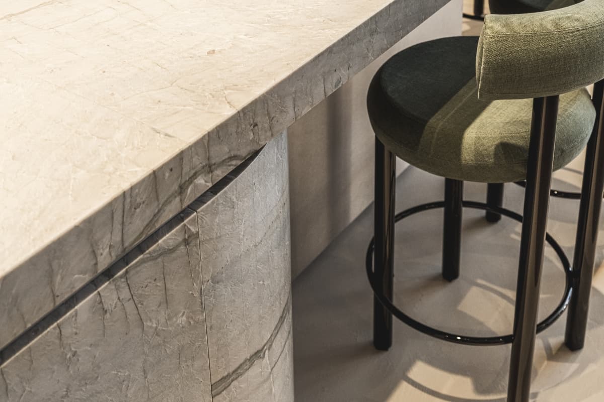 Keukeneiland van beige marmer met een groen barkruk met zwarte poten