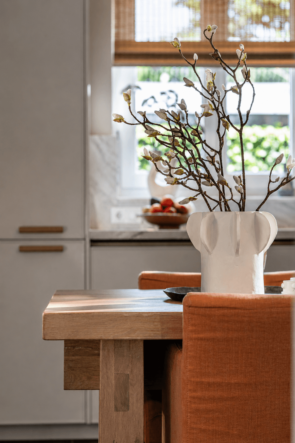 Hoek van een houte tafel met daarop een witte pot met takken